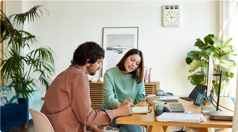 Un homme et une femme sont assis à un bureau et examinent des notes ensemble. La femme pointe un stylo sur une page et l’homme suit du regard.