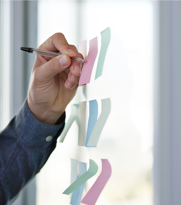 Le bras gauche d’une personne écrit des notes sur des Post-it placés sur une cloison vitrée.