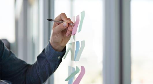Le bras gauche d’une personne écrit des notes sur des Post-it placés sur une cloison vitrée.